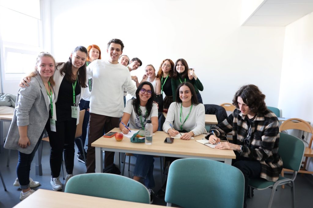 Polish language course participants, some sitting at a desk and some standing posing for a photo