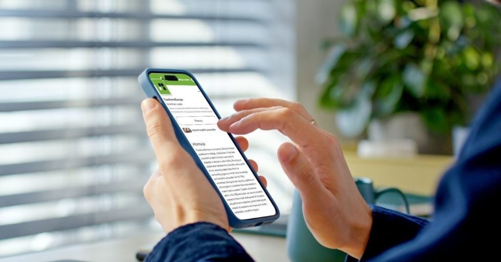 A person holds a smartphone and scrolls through a news article or document. The background shows blurred blinds and a green plant, creating a calm indoor setting.