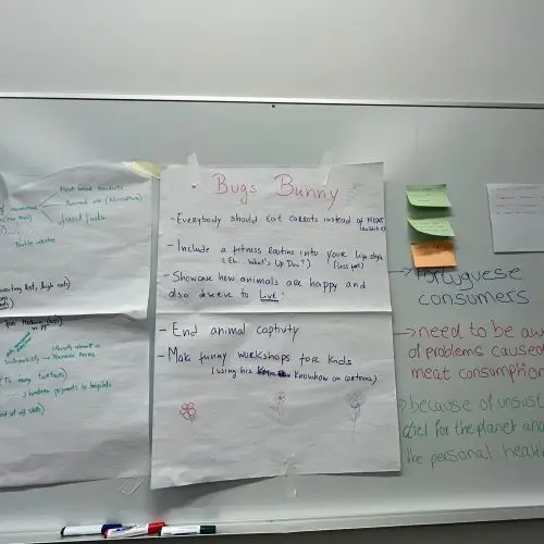 A whiteboard with handwritten notes and posters. One poster titled Bugs Bunny suggests eating carrots instead of meat and ending animal captivity. Notes about Portuguese consumers and the impact of meat consumption are on the right.