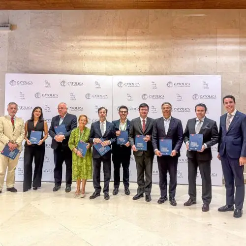 A group of ten people dressed in formal attire stand indoors, holding certificates, posing for a photo in front of a backdrop with the Cátolica logo and text.
