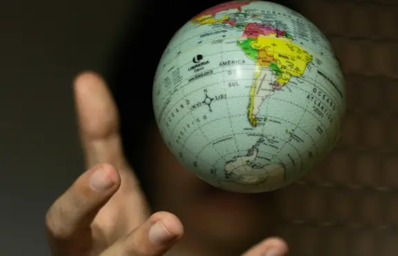 A hand reaches out towards a small globe showing South America, with the globe appearing to float in midair against a blurred background.