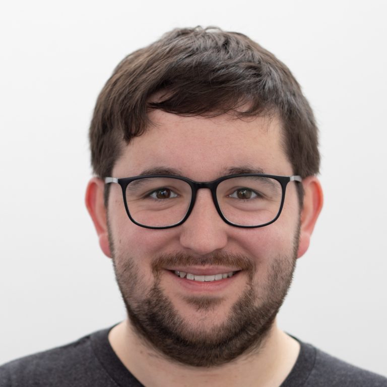 A man with short brown hair, glasses, and a beard is smiling at the camera against a plain white background, embodying the spirit of Transform for Europe.