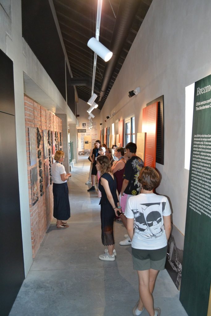 A group of people stands in a museum hallway, listening to a tour guide. Exhibits and informational panels line the walls. The atmosphere is bright and attentive.