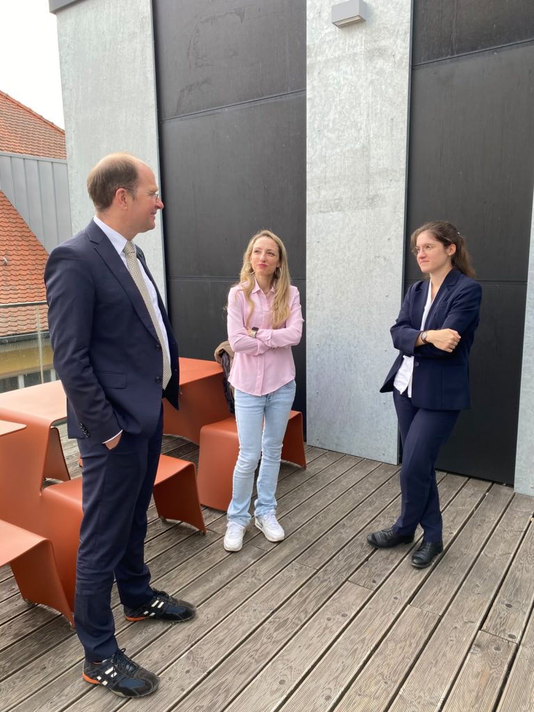 A man in a suit and sneakers stands on a deck talking to two women standing nearby.
