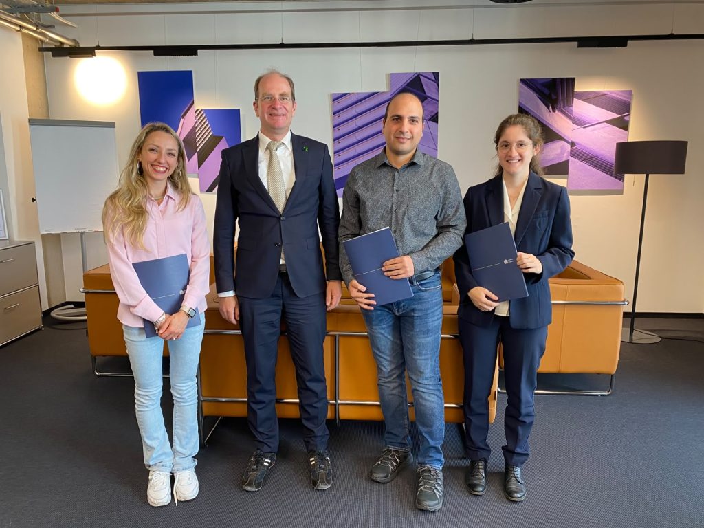 Four people standing in an office, each holding a blue folder.