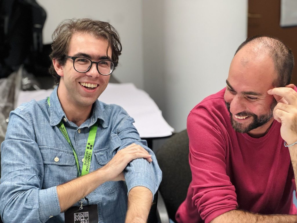 Two men laughing and talking together at a desk.
