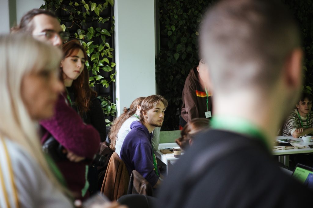 A group of people sitting at tables in a room with a vertical indoor garden.