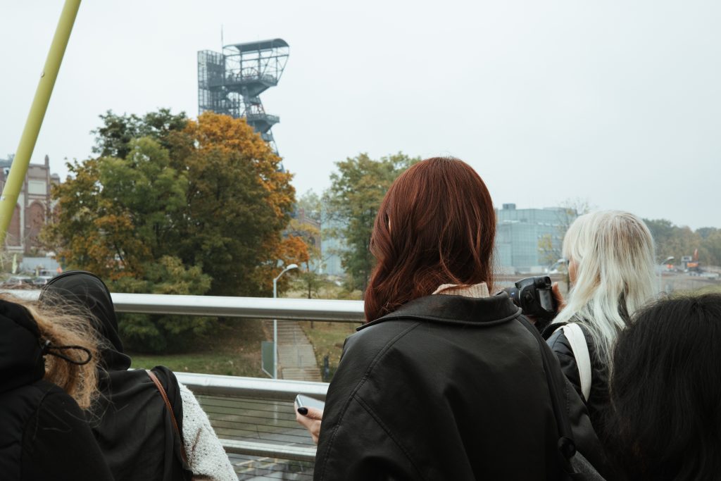 A group of people look out over a railing toward a tall industrial structure in the distance.