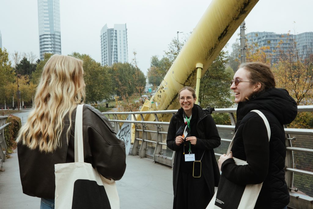 Three people stand on a bridge, talking and smiling at each other.