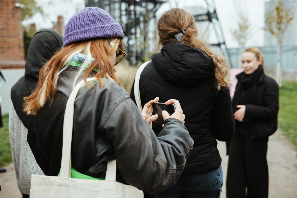 A person in a purple beanie holds up a smartphone to take a photo of another person standing nearby.