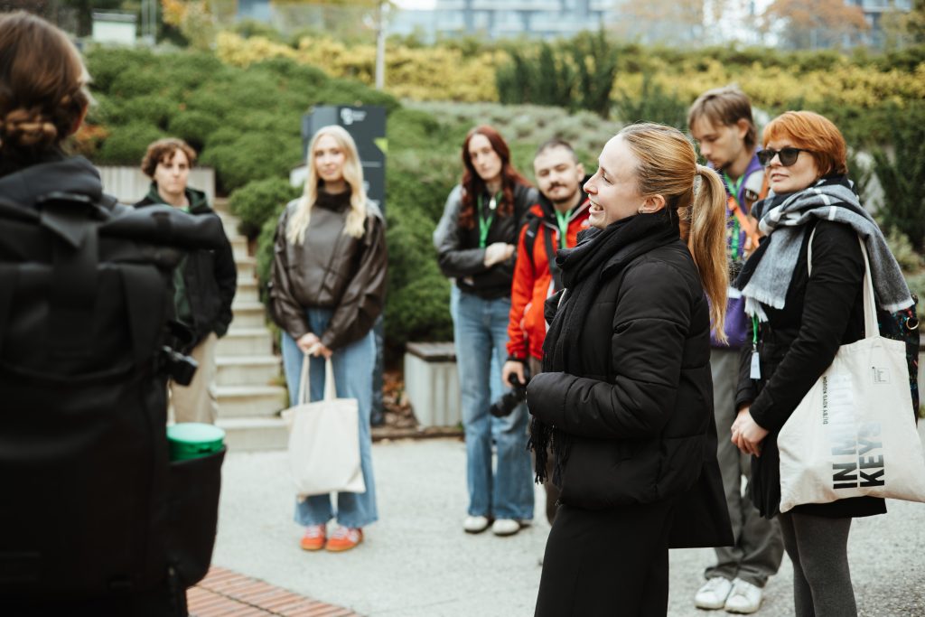 A group of people standing outdoors listening to a person speaking off-camera.
