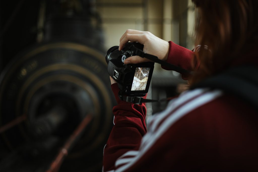 A person in a red sweatshirt holding a camera to take a photo of large industrial machinery.