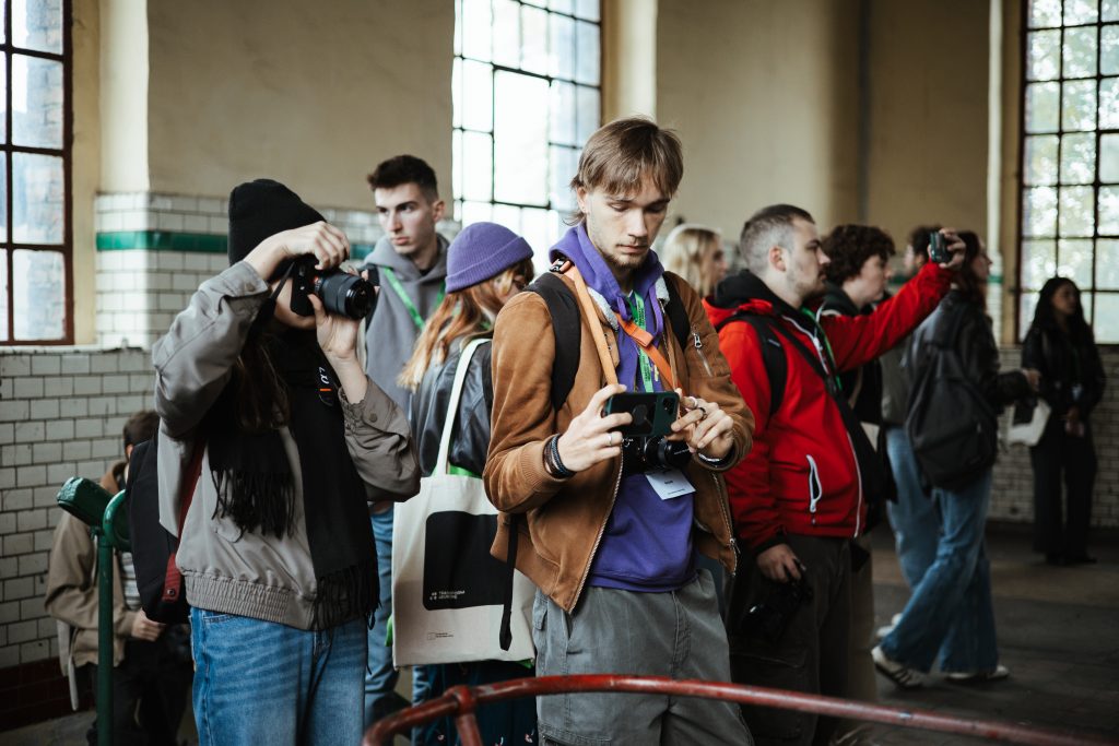 A group of people standing in a building, some holding cameras and phones to take pictures.