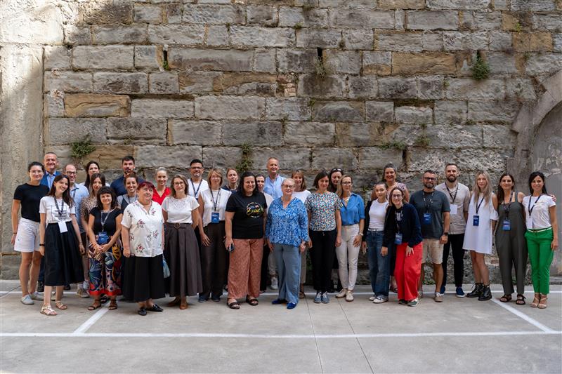 A large group of people stand in a line against a stone wall for a group photo.