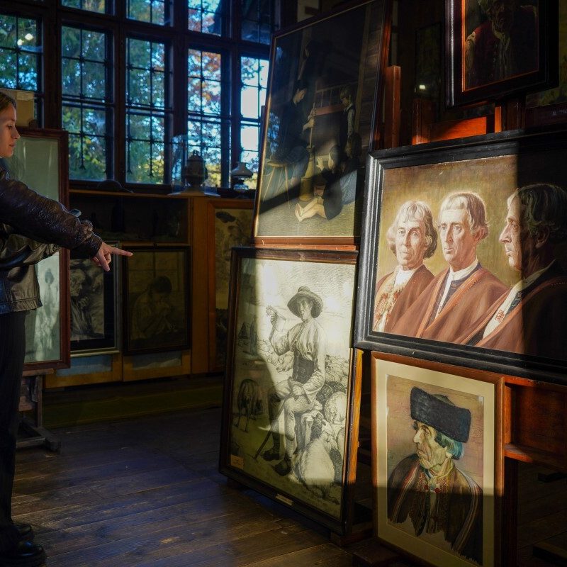 A person pointing to one of four paintings hanging on a wall